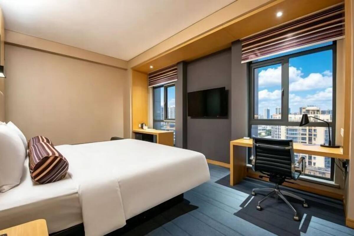 Hotellihuone, jossa on suuri sänky, työpöytä, tuoli, televisio ja ikkuna, josta avautuu näkymä kaupunkiin.