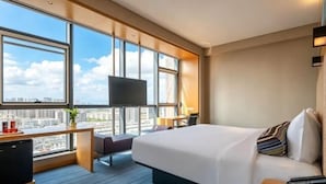 A hotel room with a large bed, a desk, a TV, and a view of the city. - Yancheng Baolong Yiyue Select Hotel (Yancheng)