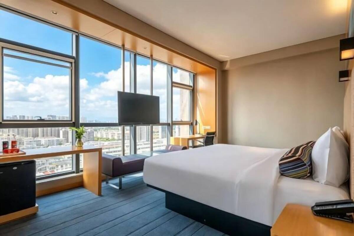 Hotellihuone, jossa on suuri sänky, työpöytä, televisio ja näkymä kaupunkiin.
