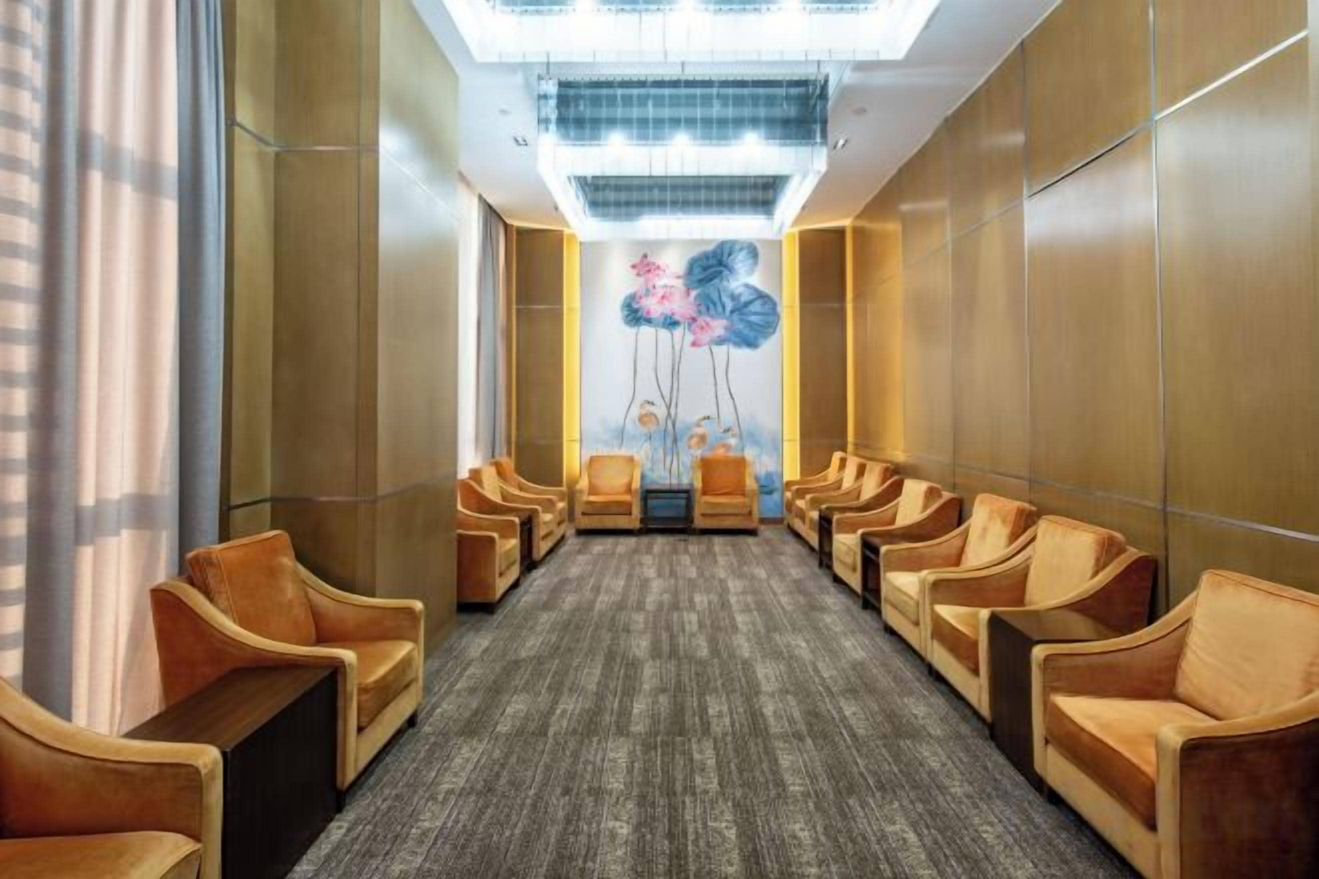 Un vestíbulo de hotel con una fila de sillones de cuero, piso alfombrado y un cuadro colgado en la pared.