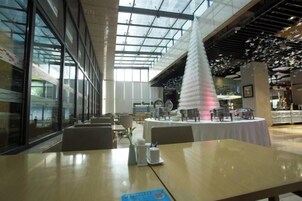 A restaurant with a high ceiling and large windows, featuring a central white column and tables set for dining.
