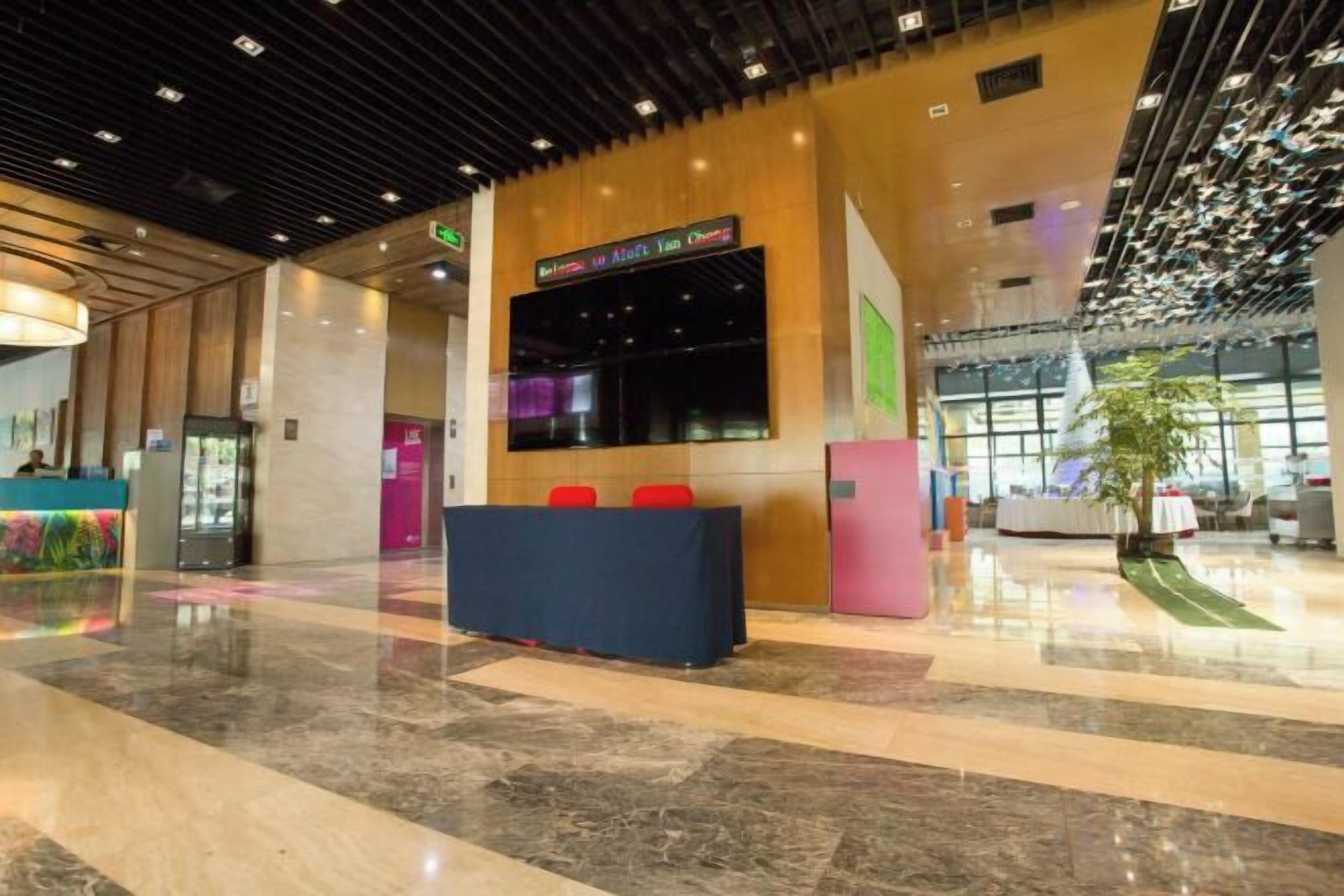 Un vestíbulo amplio con mostrador de recepción, zona de estar y una pantalla digital grande.