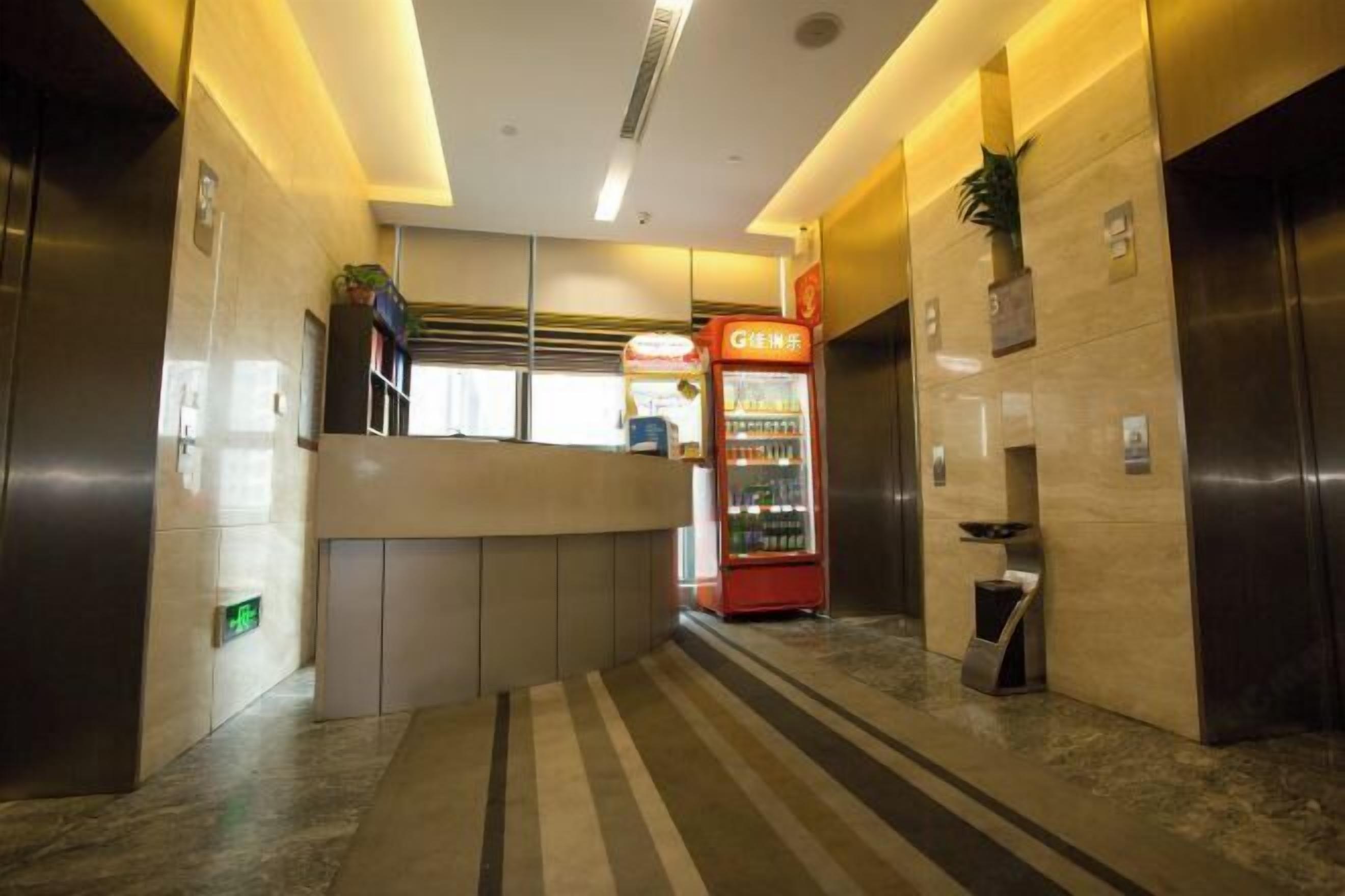 A modern hotel lobby with a reception desk, vending machine, and elevators.
