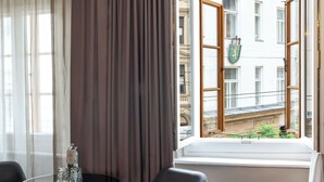 A hotel room with a round table, two chairs, a window with curtains, and a view of buildings outside. - Aiola Living Boutique Hotel Graz (Graz)