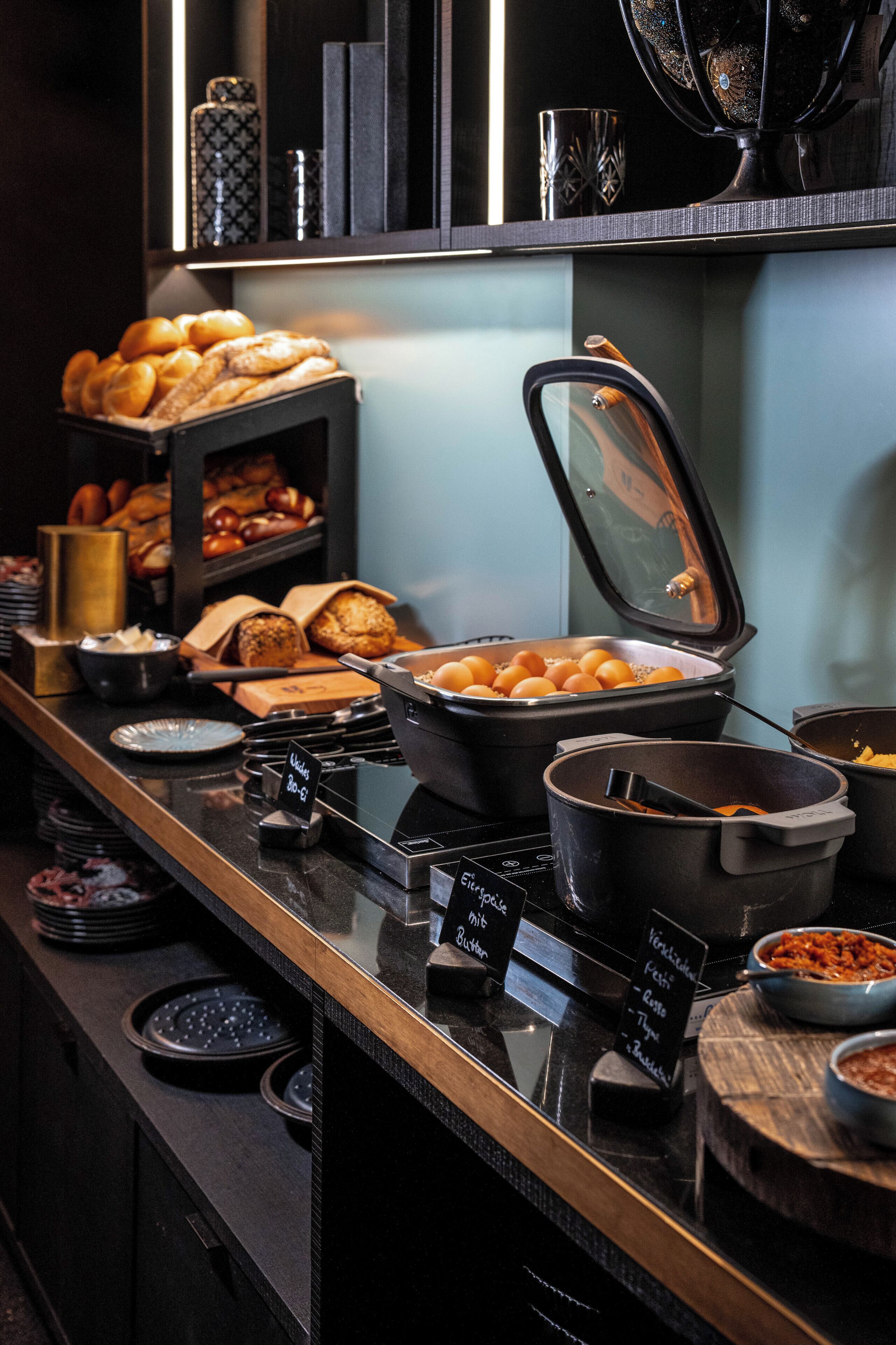 A buffet counter with various food items, including bread, pastries, and a hot food station.
