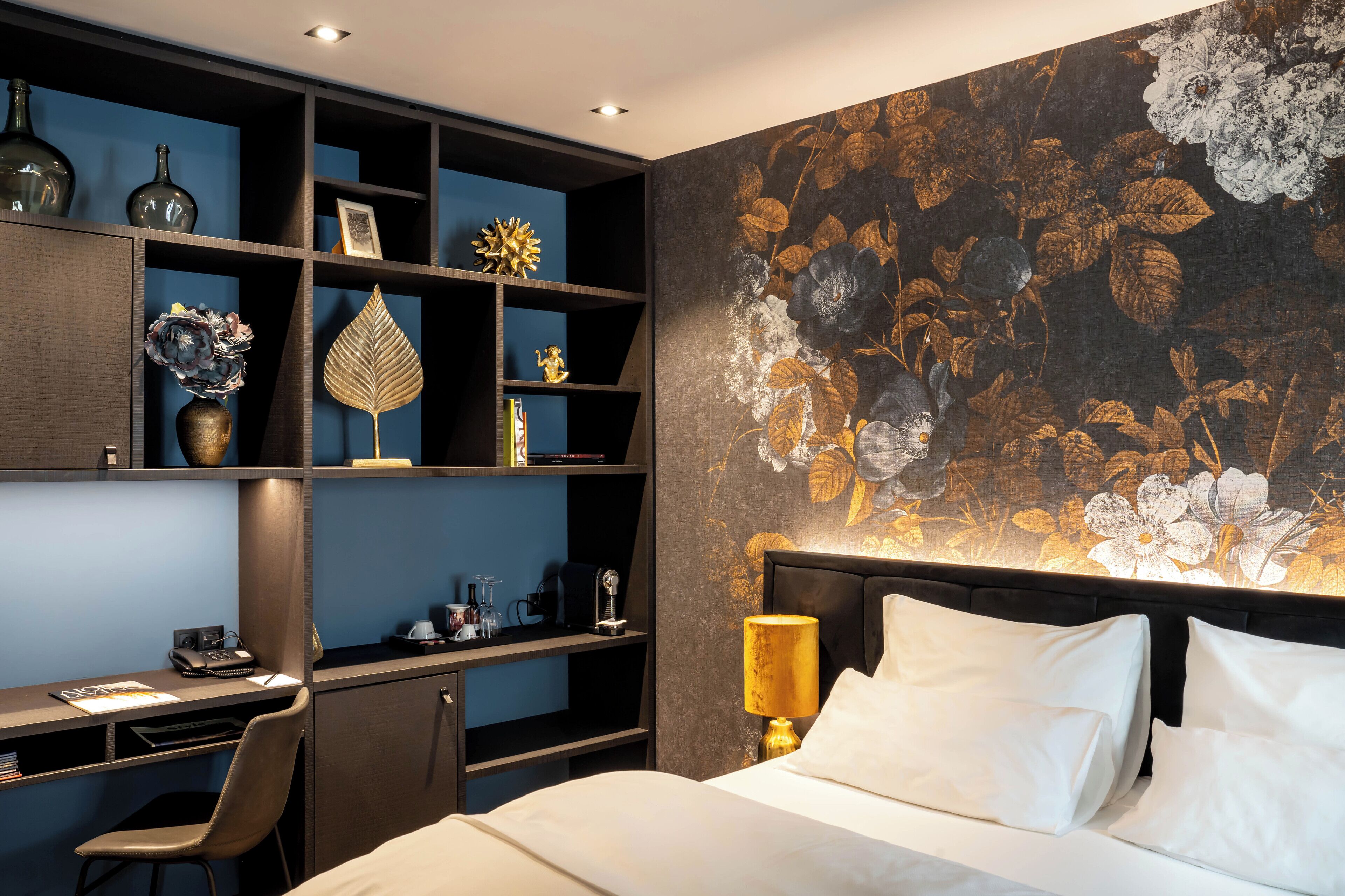Una habitación de hotel con una cama, un escritorio y una estantería con objetos decorativos.