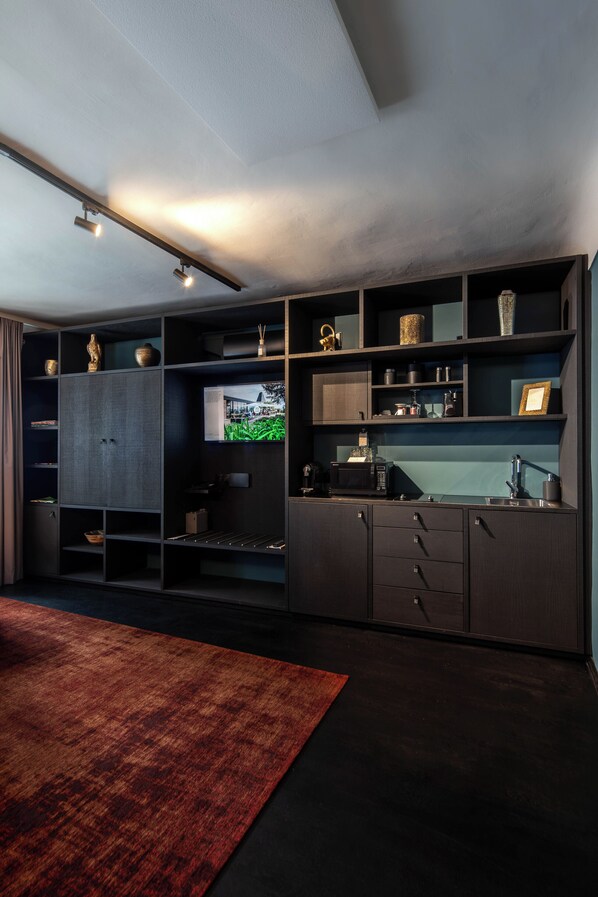 A modern kitchen with built-in appliances, dark cabinetry, and a flat-screen TV.