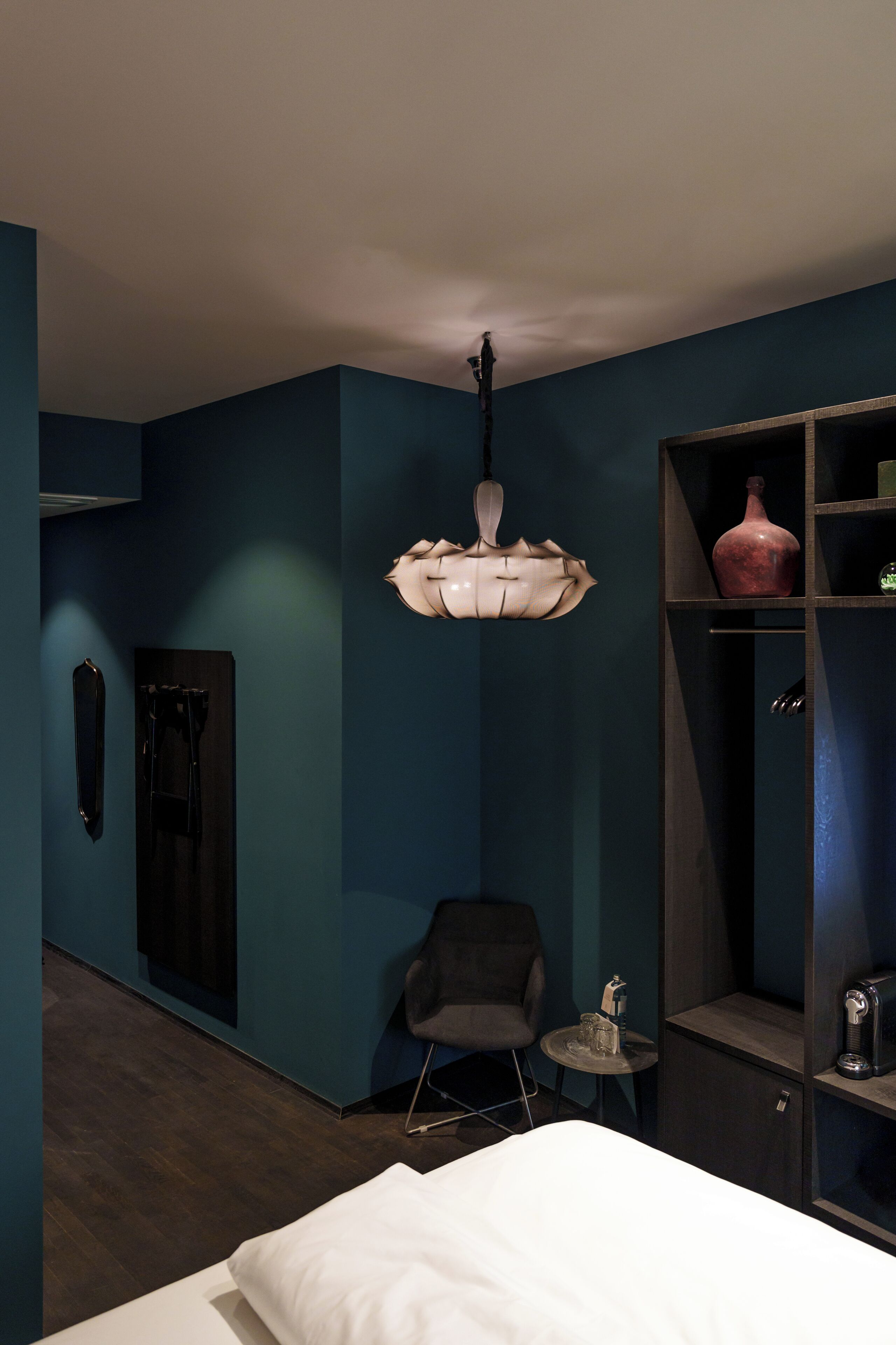 Una habitación de hotel moderna con una cama, una silla, una mesita y un mueble decorado con objetos decorativos.