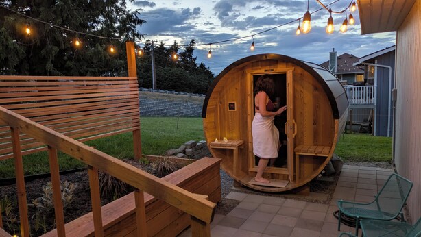 A wooden sauna with a bench and a small table, surrounded by a wooden deck and outdoor lighting. - Sauna, Beach, Sunset, Game Room, Peace and Quiet, Fun! (Oak Harbor)