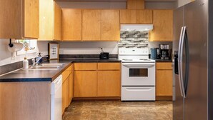 A modern kitchen with wooden cabinets, a stainless steel refrigerator, a white stove, and a tiled backsplash. - Sauna, Beach, Sunset, Game Room, Peace and Quiet, Fun! (Oak Harbor)