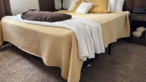 Una cama bien hecha con un edredón color beige, una manta marrón y almohadas blancas.