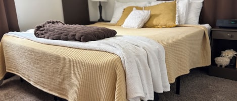 En snyggt bäddad säng med ett beige täcke, en brun pläd och vita kuddar.
