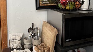Una encimera de cocina con un cuadro enmarco que muestra una escena de canal, un bol de fruta y diversos utensilios de cocina.