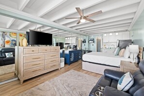 A spacious room with a large bed, a wooden dresser, a television, and a ceiling fan.