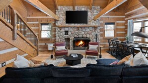 A log cabin interior with a stone fireplace, wooden walls, a flat-screen TV, a dining area, and a cozy seating area with a sofa and chairs. - Amber Hills Lodge: Sauna,Golf Sim,Hot Tub,Theatre (Lancaster)