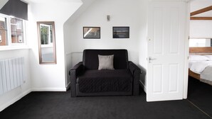 A room with a black sofa, a white door, and two framed pictures on the wall. - Cosy Family One Bedroom flat with private Kitchen (Sutton)