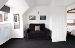 A room with a black sofa, a white door, and two framed pictures on the wall.