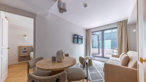 A modern living room with a round wooden table, two chairs, a sofa, and a TV on the wall.