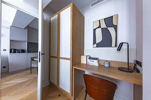 Una habitación moderna con un escritorio de madera, una silla, una estantería, un cuadro y una zona de cocina.