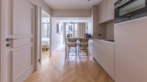 A modern kitchen with a built-in oven, a dining area with two chairs, and a view of a balcony. - Opera - One Bedroom Balcony (Paris)