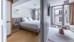 A modern hotel room with a bed, bedside tables, a TV, a window with a view of the city, and a balcony. - Opera - One Bedroom Balcony (Paris)