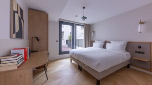 A modern bedroom with a bed, a desk with books, a wardrobe, and a view through a glass door.
