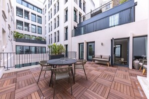 A courtyard with a round table and chairs, a sofa, and a potted plant. - Opera - One Bedroom Terrace (Paris)
