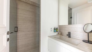 Et badeværelse med bruser, håndvask med spejl og toiletartikler på bordet.