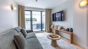 A modern living room with a sofa, a coffee table, a TV, and a balcony with curtains. - Opera - One Bedroom Balcony (Paris)
