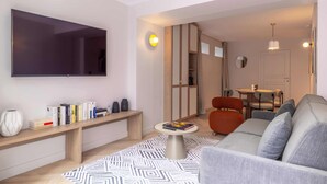 A modern living room with a flat-screen TV, a sofa, a coffee table, and a bookshelf. - Opera - One Bedroom Balcony (Paris)