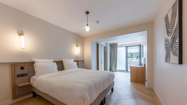 A modern hotel room with a large bed, bedside tables, a wardrobe, a desk, and a view to the outside. - Opera - One Bedroom Balcony (Paris)