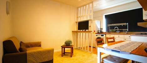 A compact living space with a sofa, a small table, a kitchen area with a microwave, and a window.