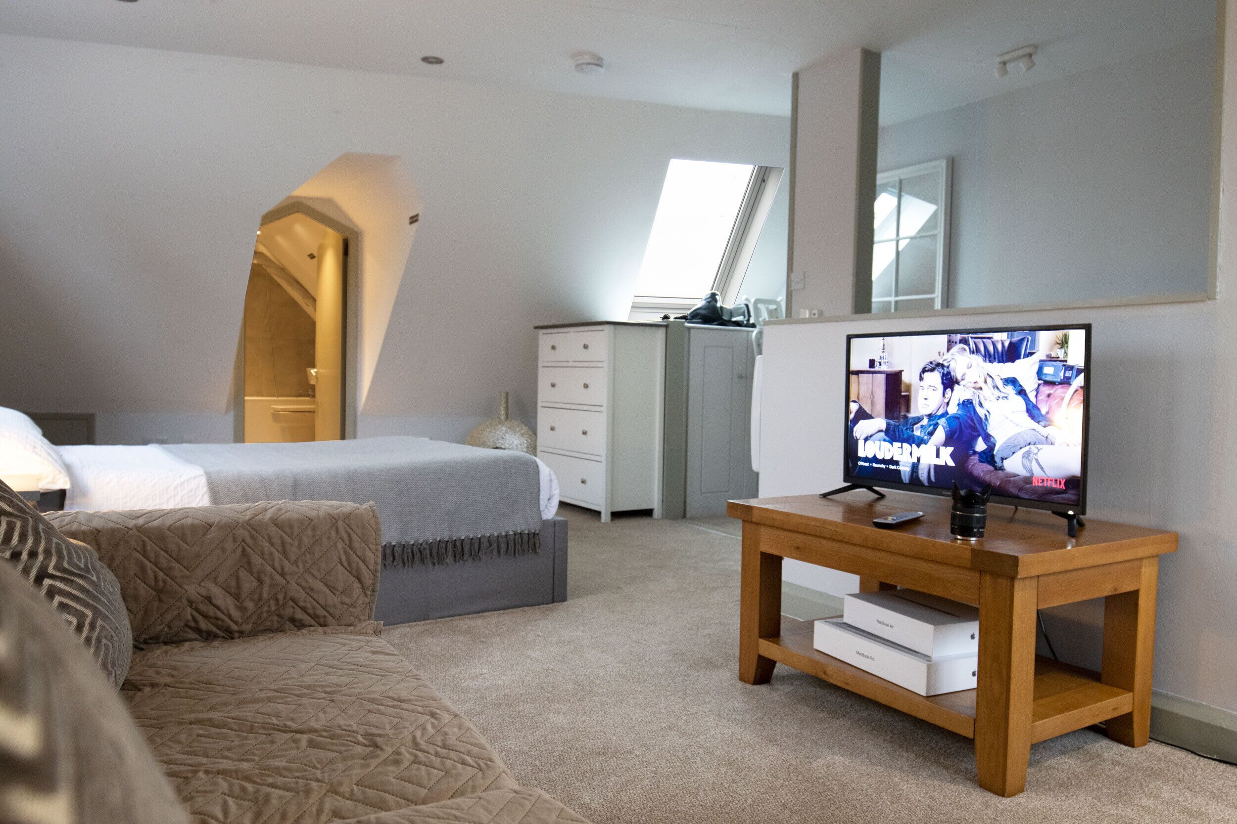 A bedroom with a bed, a dresser, a TV on a wooden table, and a large mirror on the wall.