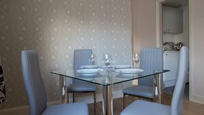 A dining area with a glass table, four blue upholstered chairs, and a patterned wallpaper.
