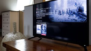 A television displaying the movie 'Society of the Snow' with a snowy landscape and a group of people.