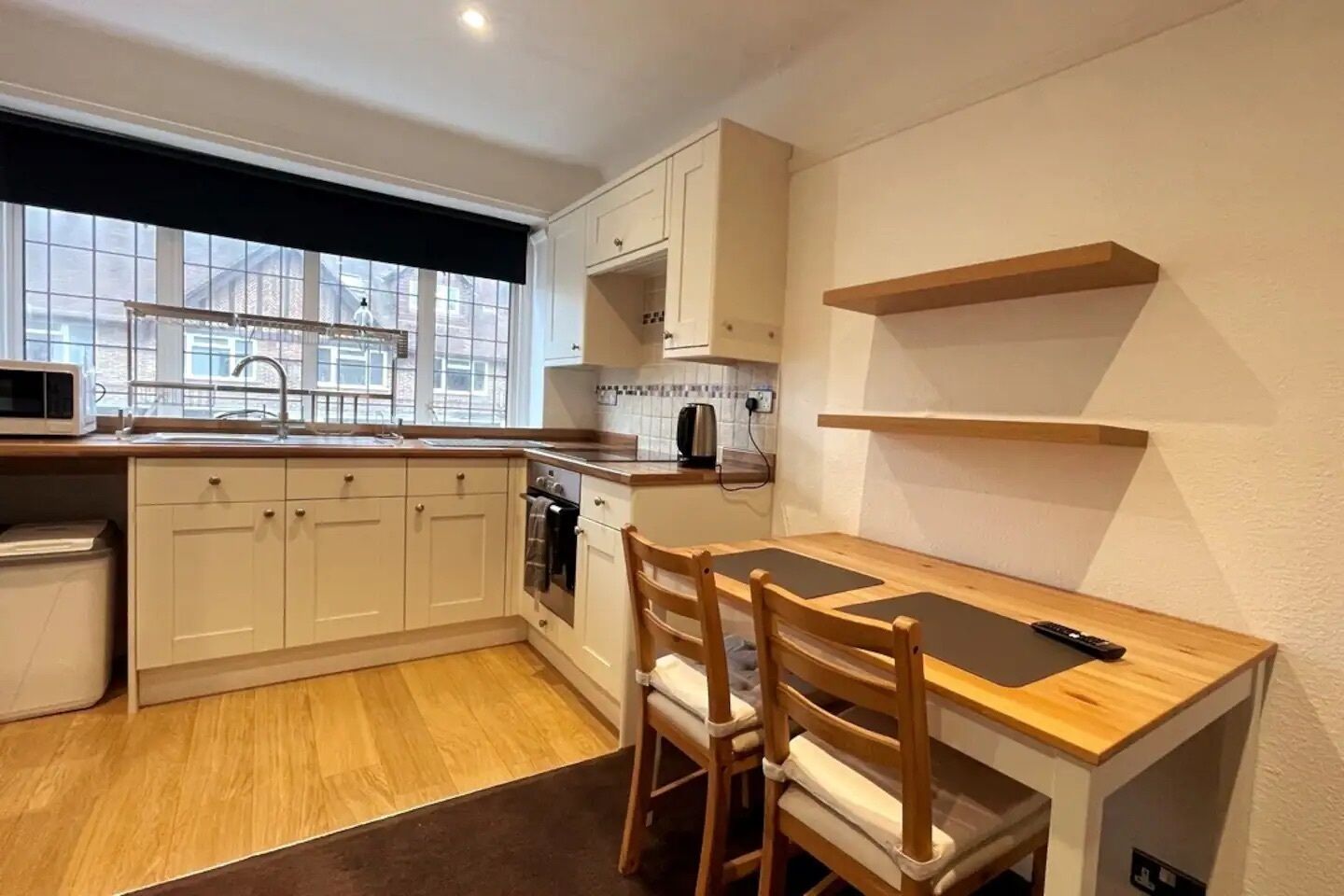 A compact kitchen with white cabinets, a wooden countertop, and a window with a black blind.