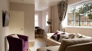 A living room with a purple armchair, a beige sofa, and a large window with a view of buildings.
