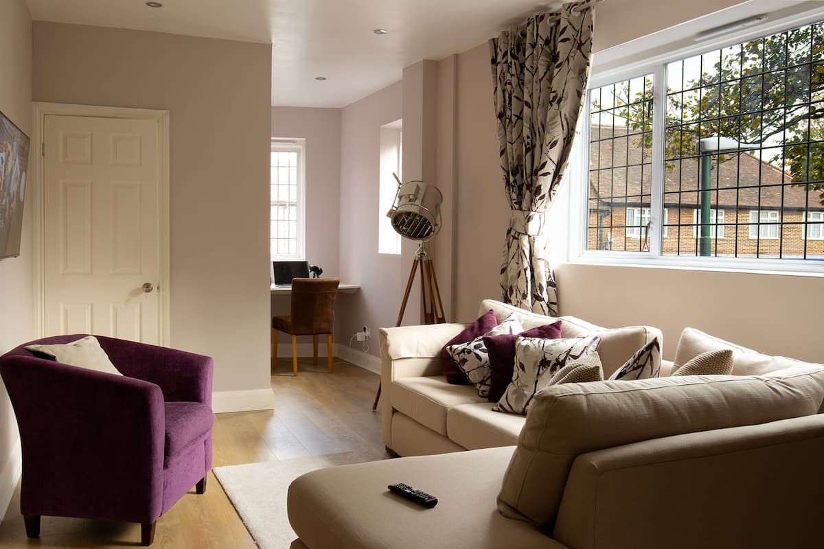 A living room with a purple armchair, a beige sofa, and a large window with a view of buildings.