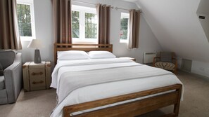 A bedroom with a wooden bed, a nightstand, a lamp, a chair, and a window with curtains. - Straight Inn (Sutton)