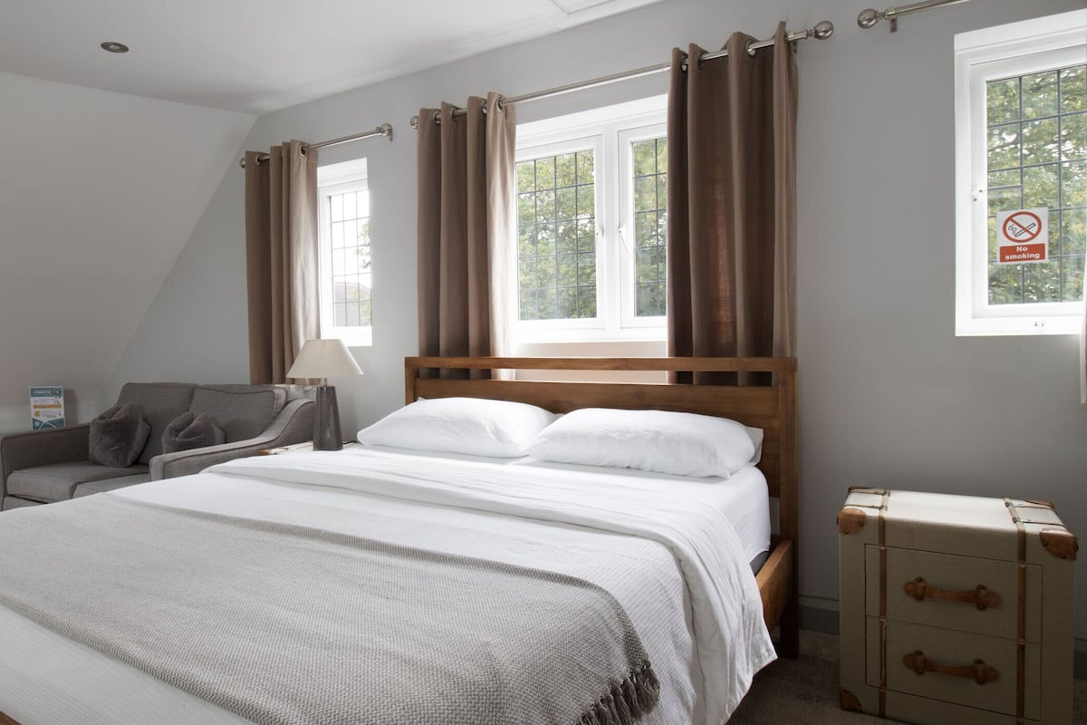 A bedroom with a bed, a nightstand, a chair, a suitcase, and a window with curtains.