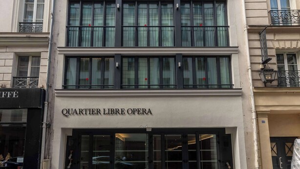 A building with a modern facade, multiple windows, and a sign reading 'QUARTIER LIBRE OPERA'.