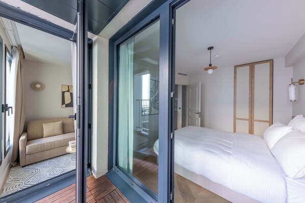 A bedroom with a bed, a sofa, and a sliding glass door leading to a balcony.