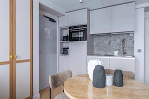 A compact kitchen with built-in appliances, a dining area with a round table and chairs, and a grey backsplash.