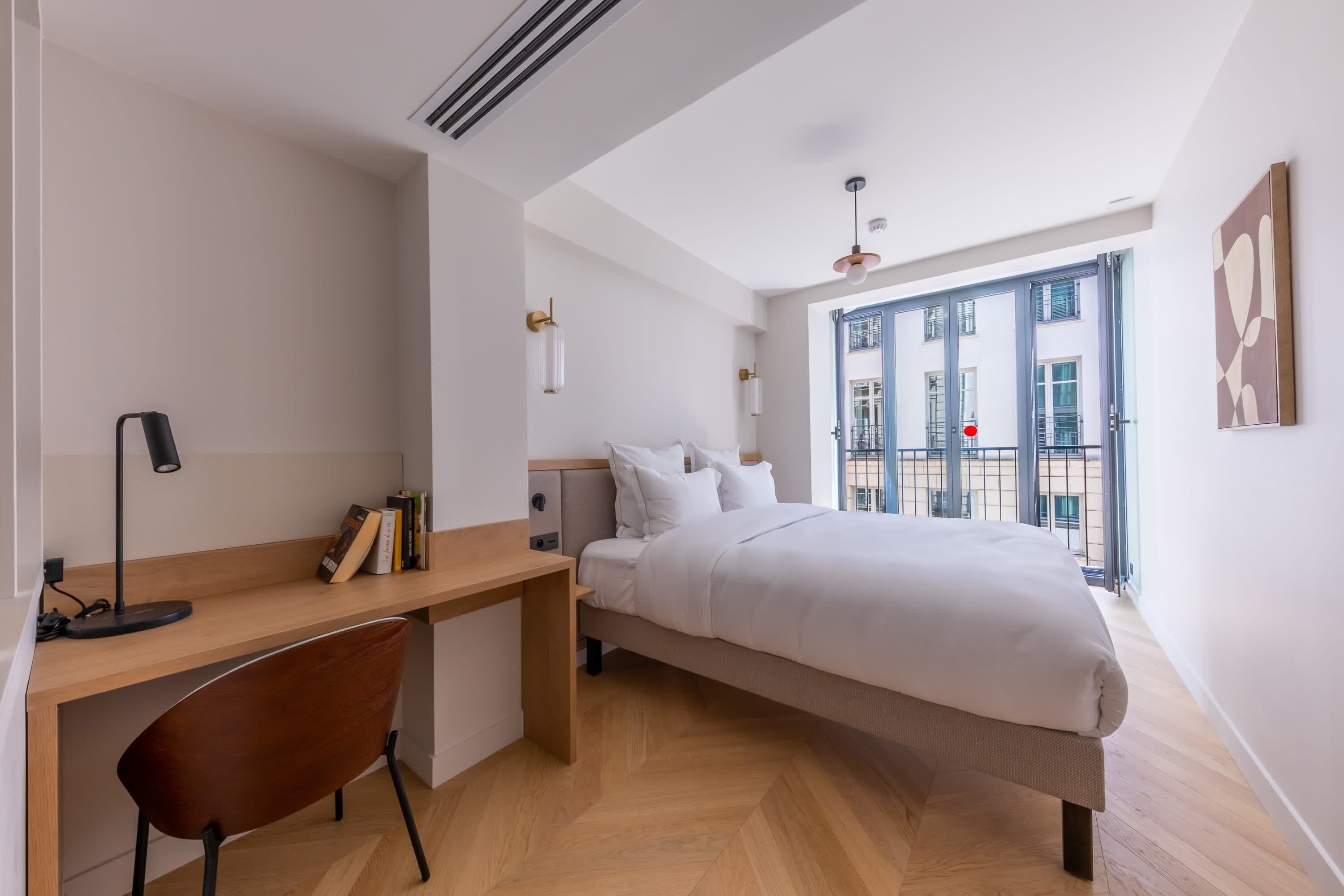 Un dormitorio con cama, escritorio, silla y ventana grande.