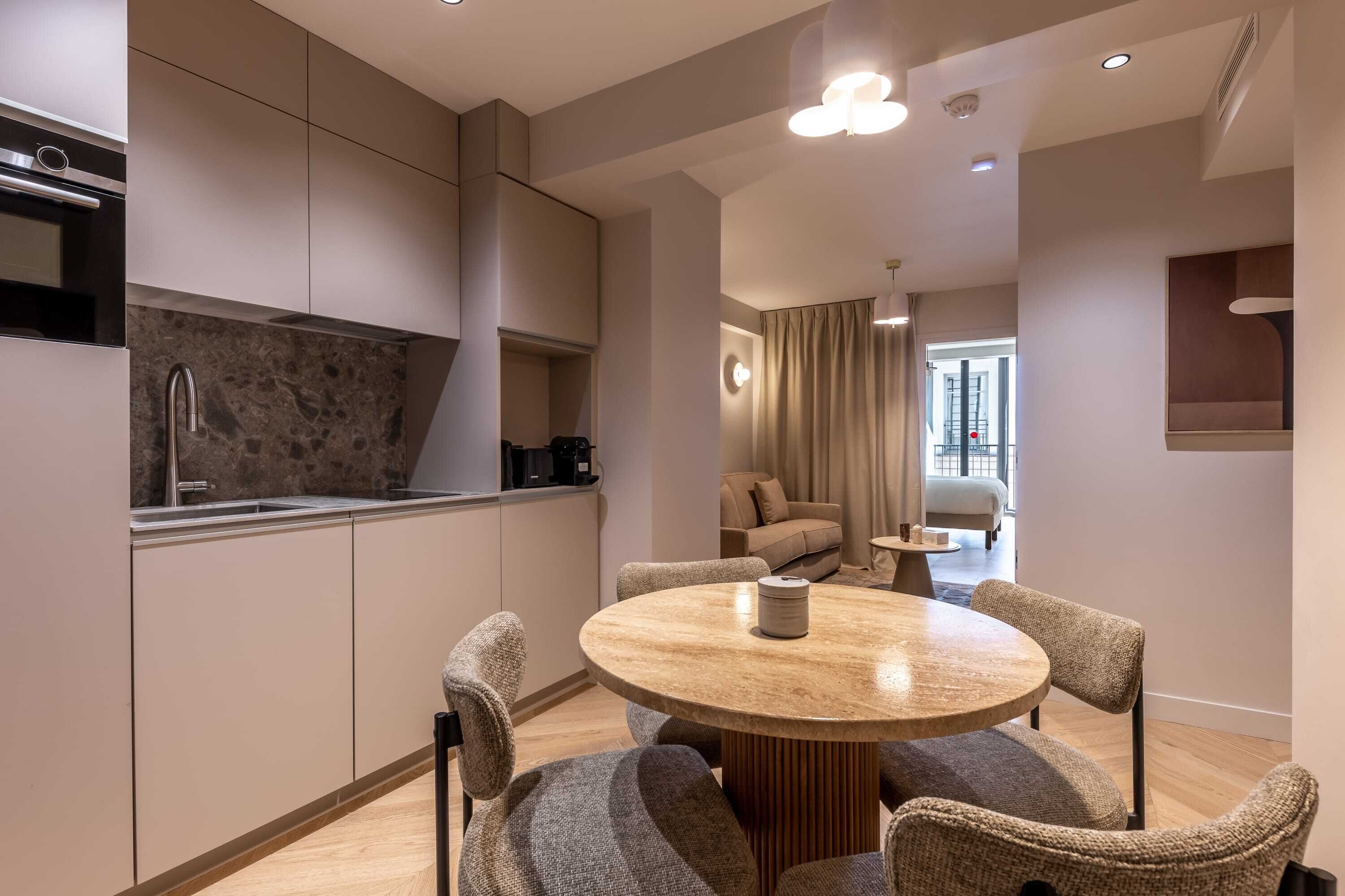 Una cocina moderna con estufa integrada, un comedor con mesa redonda y cuatro sillas, y una sala de estar con sofá y mesa de centro.