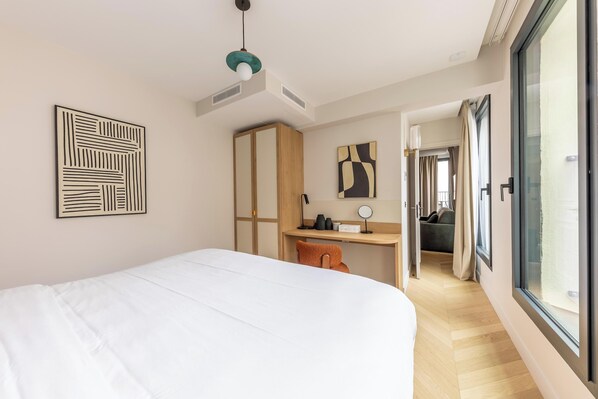A bedroom with a bed, a desk, a chair, a wardrobe, a mirror, and a window.