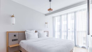 Une chambre à coucher moderne, dotée d’un grand lit, de tables de chevet et offrant une vue sur l’extérieur à travers de fines rideaux.