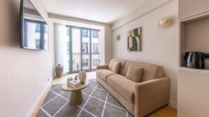 Un salon comprenant un canapé, une table basse, un téléviseur à écran plat, une grande fenêtre et un balcon.