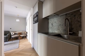 A modern kitchen with a stone backsplash, stainless steel appliances, and a dining area with a round table and chairs. - Opera - One Bedroom Balcony (Paris)
