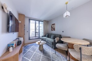 A modern living room with a sofa, a round table, a TV mounted on the wall, and a bookshelf. - Opera - One Bedroom Balcony (Paris)
